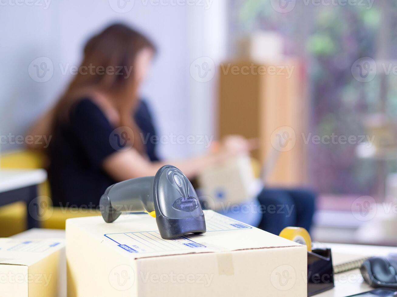 Close-up of reader barcode on parcel box in the office with young couple blurred background. Easy startup e-commerce and shipping service. Space for text. Business online concept photo
