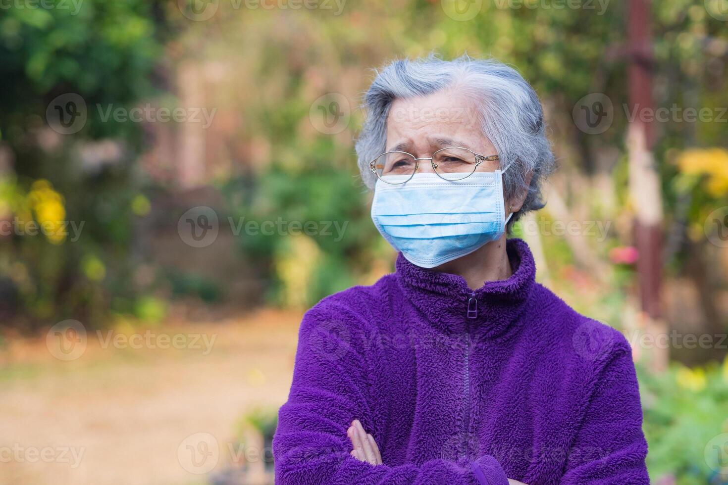 Portrait of elderly Asian woman wearing a face mask and arms crossed while standing in the garden. Mask for protection virus, Covid-19, Coronavirus. Concept of aged people and healthcare photo