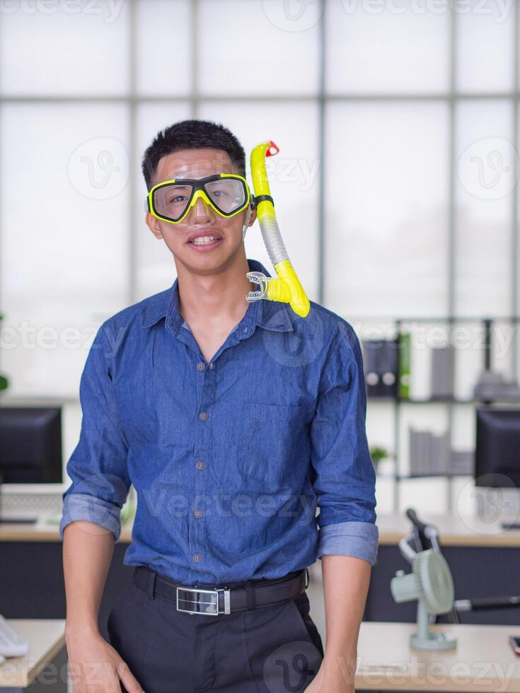 Portrait of a young man wearing a diving mask yellow, smiling and looking at the camera while standing in the office. Holiday coming soon. Holiday concept photo