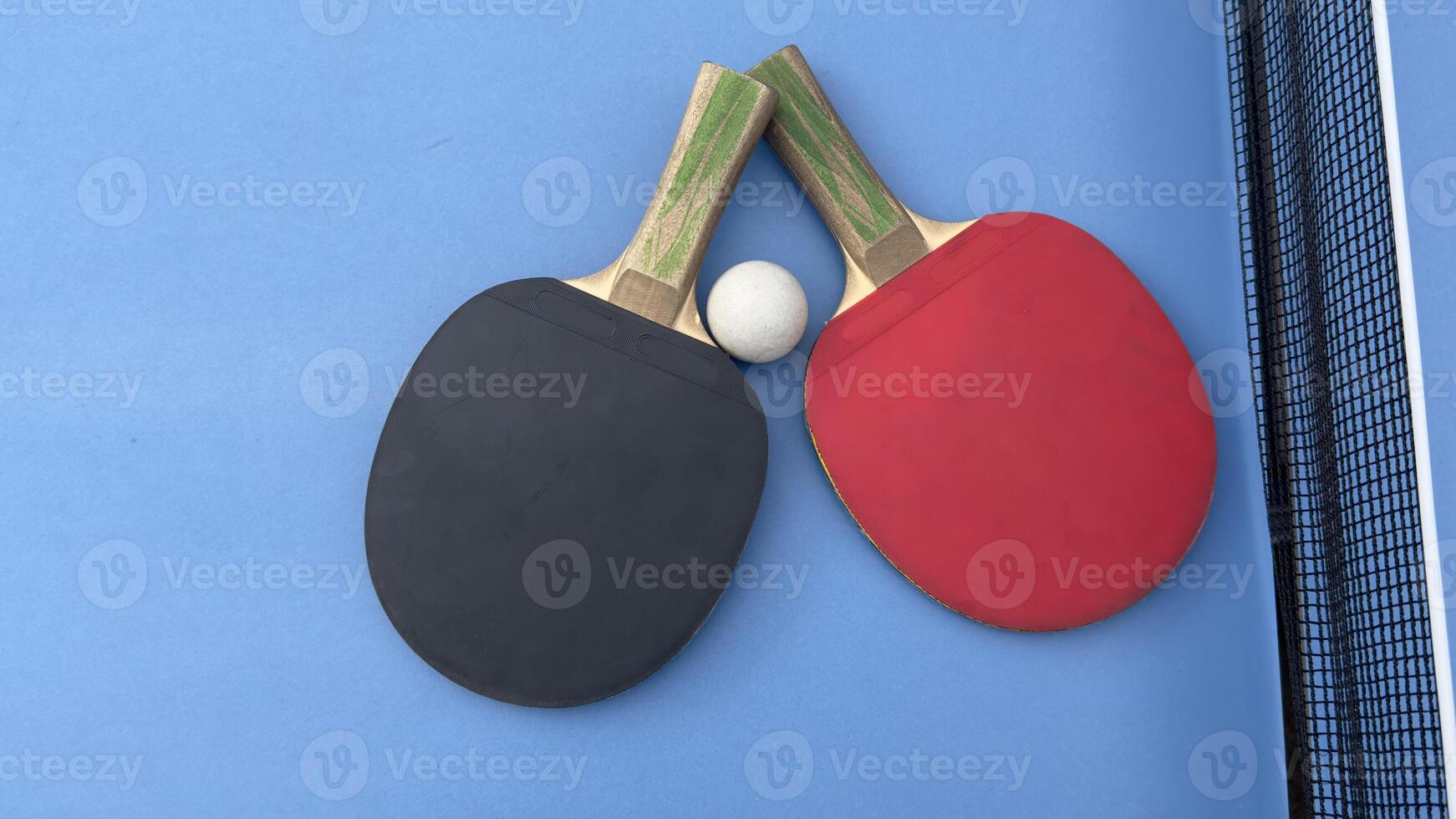 Two table tennis rackets and balls on a blue table with net. photo