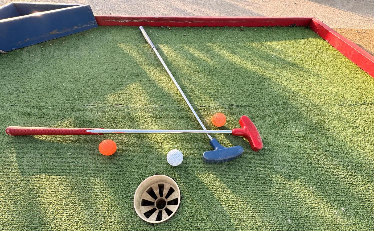Assorted miniature golf putters and balls askew on synthetic grass. photo