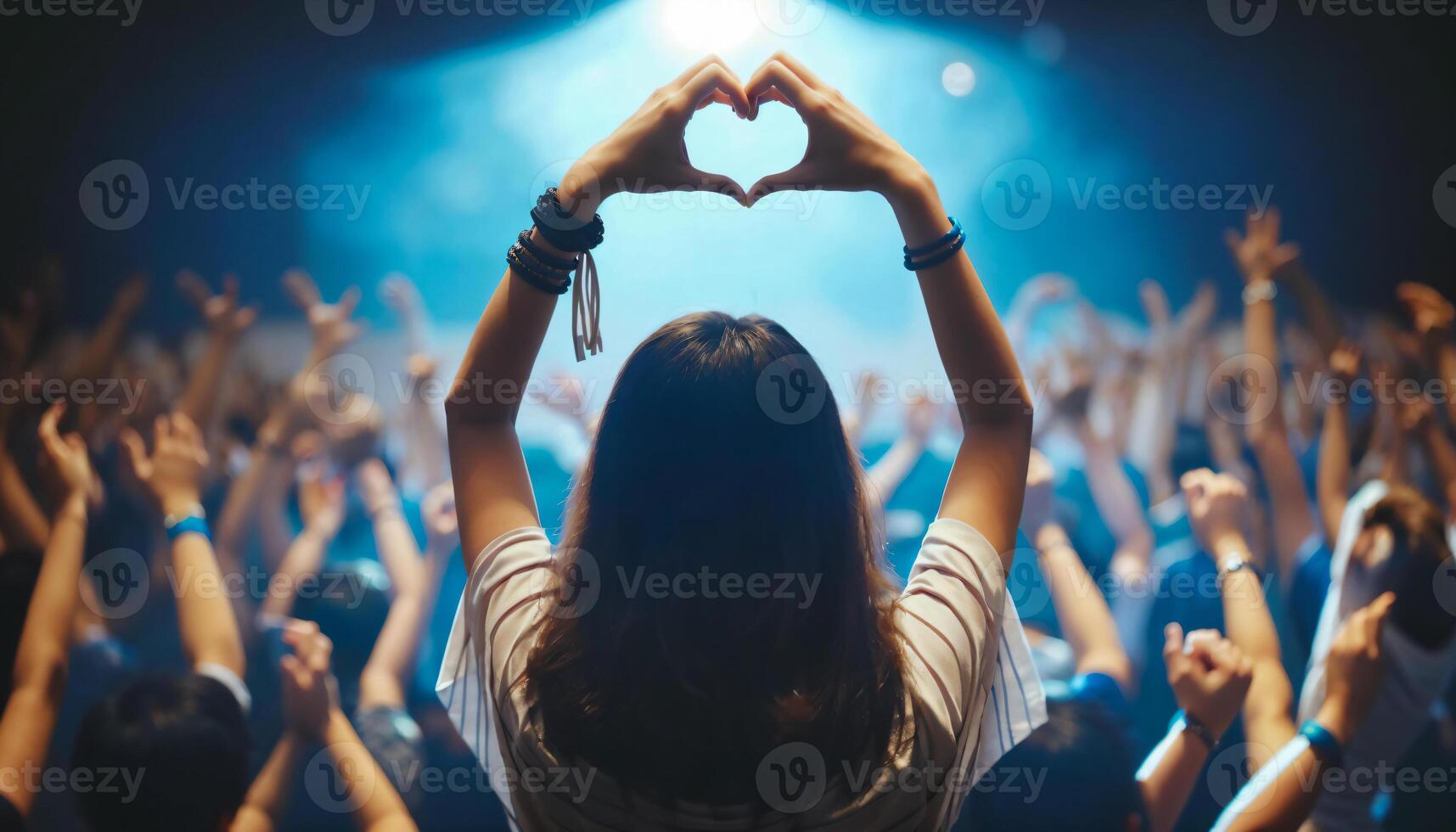 Woman Making Heart Shape at Concert with Crowd in Background photo