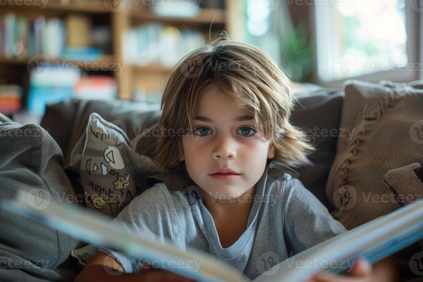 Cute boy reading a book and smiling while sitting on a sofa in the room. photo