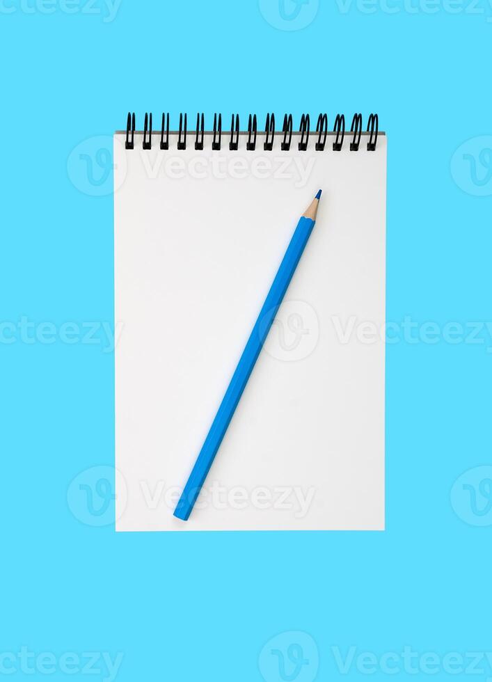 A blank notebook and a blue pencil on a blue background. Flatlay composition. Top view. photo