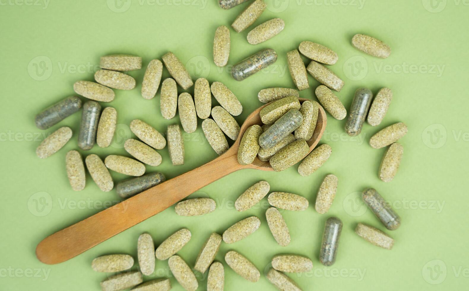 Natural supplements in a wooden spoon on a green background. Top view. Close-up. photo