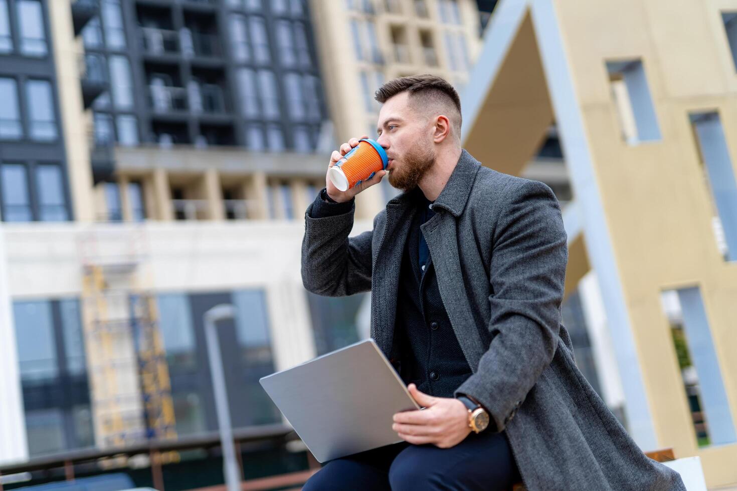 Young professional businessman in a suit using hi tech laptop outdoors. Successful manager working outdoor during a break and searching for information in internet on laptop computer. photo