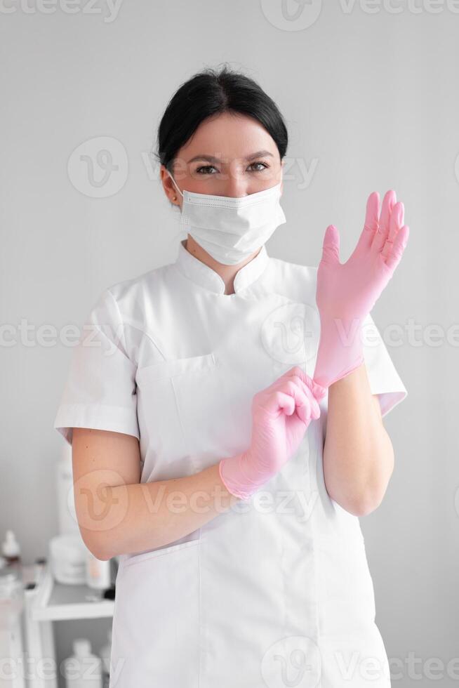 Cosmetologist in mask putting on pink gloves in beauty clinic photo