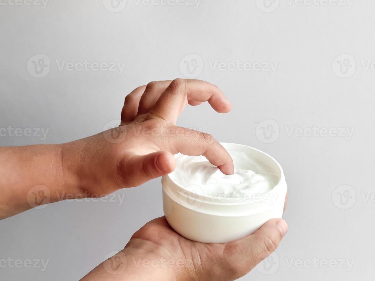 Close up of childs hands holding container of hand cream and dipping finger on white background. Skincare and moisturizing concept. Design for healthcare, wellness, and child care poster. photo