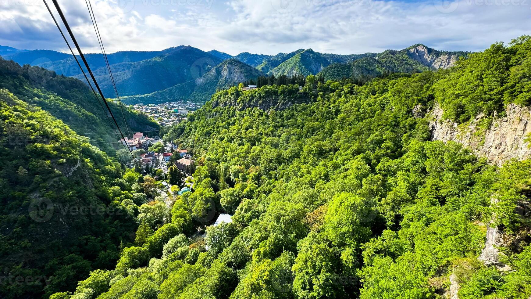 Georgia. Borjomi Historical Park. View from the cable car funicular. May 19, 2024. Scenic aerial view of lush green valley with village nestled among the mountains under sky with clouds. photo