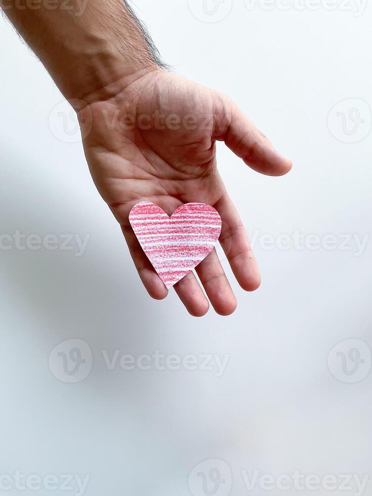 Mans hand holding striped pink paper heart against white background, symbolizing love and care, with copy space. Can be used for design and print related to childrens, love and relationships themes photo