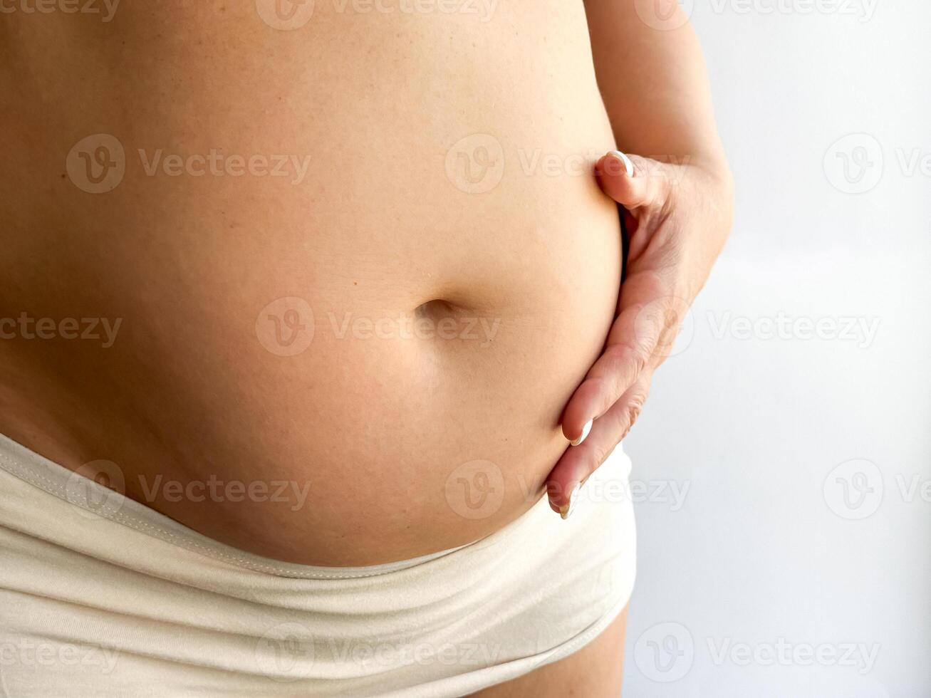 Pregnant belly in beige underwear with hand touching. Close up photography for maternity, pregnancy, and motherhood concept. Design for healthcare, prenatal care and wellness. photo