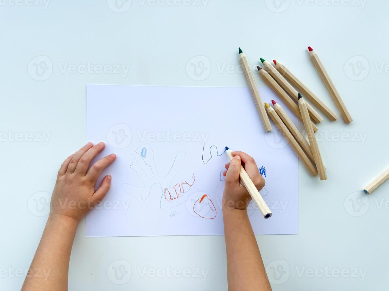 small child draws with colored pencils on paper on white table. photo