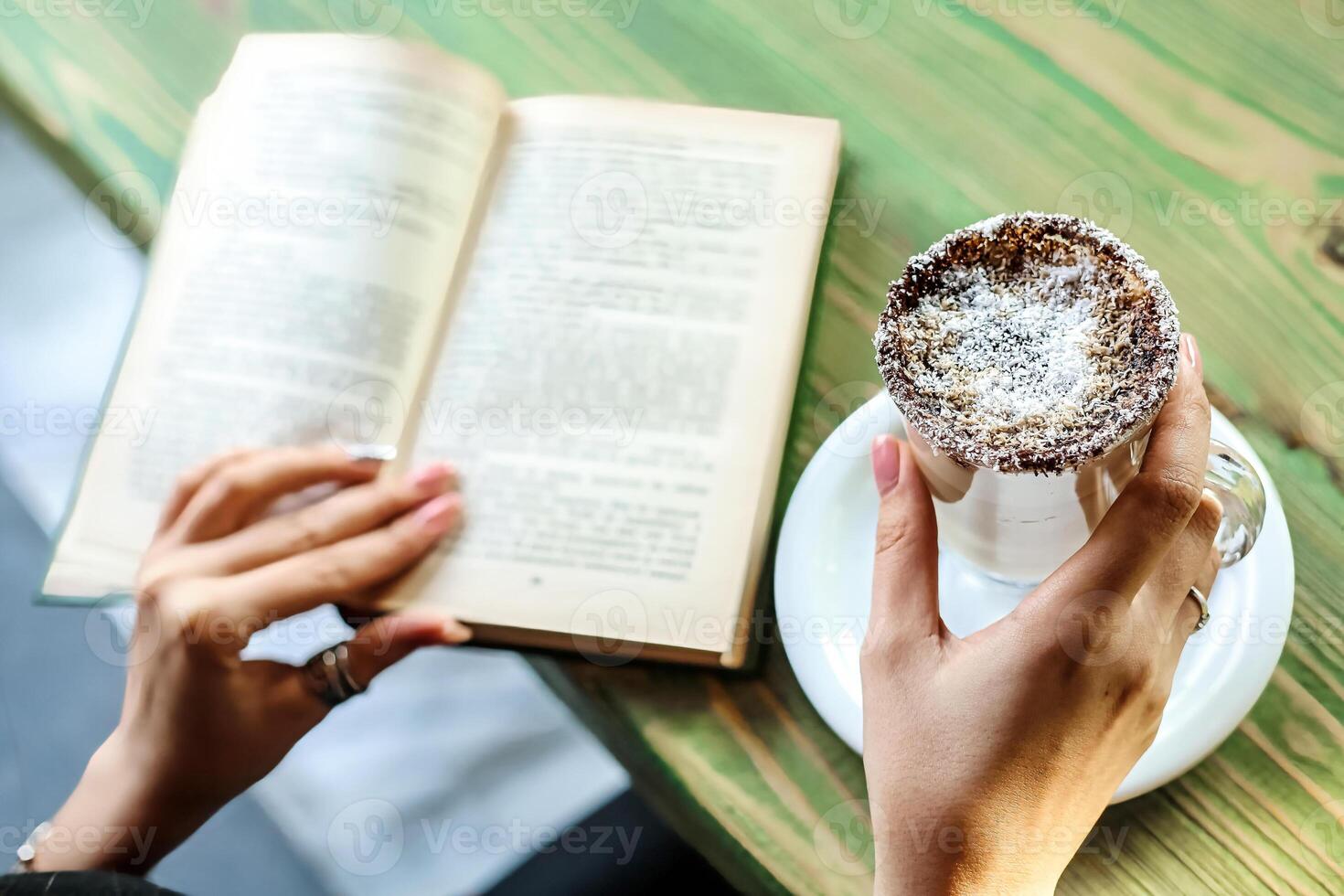 Person Reading Book and Holding Pastry at Outdoor Cafe photo