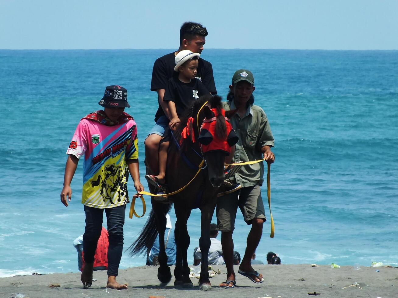Kebumen, Central Java, Indonesia April 11, 2024 People enjoy vacation riding a horse during bright daylight at Ambal Beach. Summer family tourist spot with ocean wave background. photo
