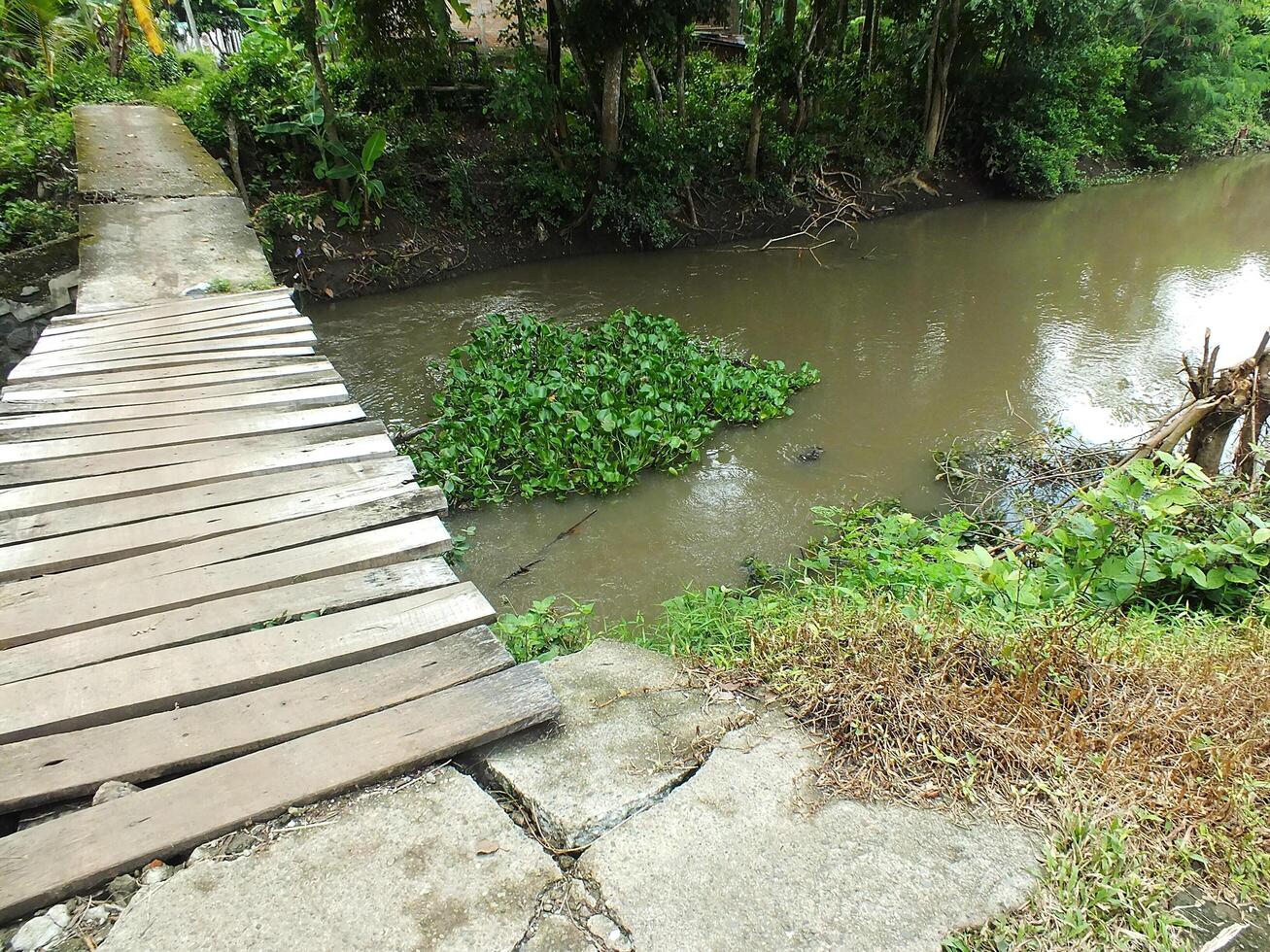 sightseeing of a rural scene with an old wooden bridge crossing a brown water river photo