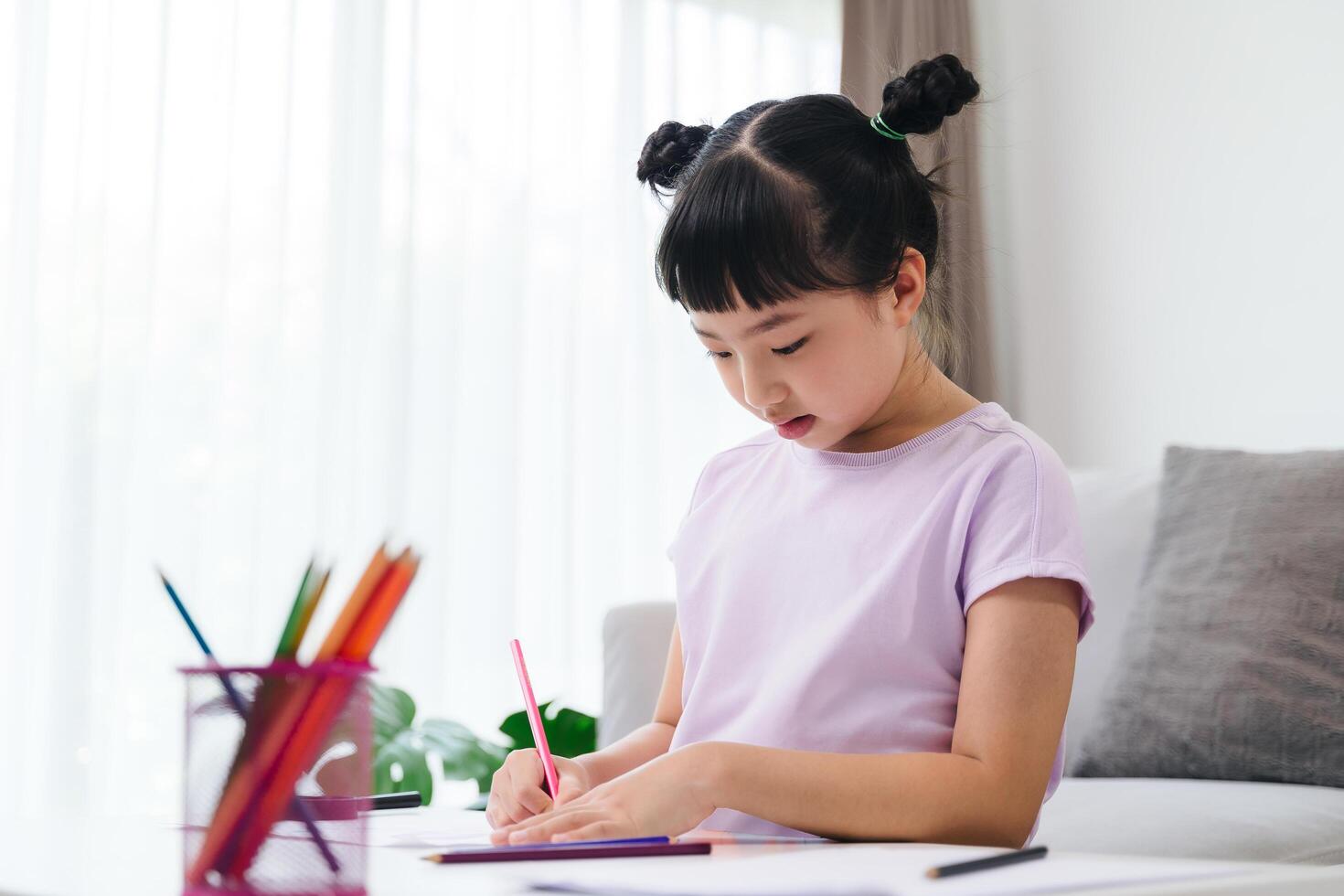 A young girl is sitting on a couch and drawing with crayons photo