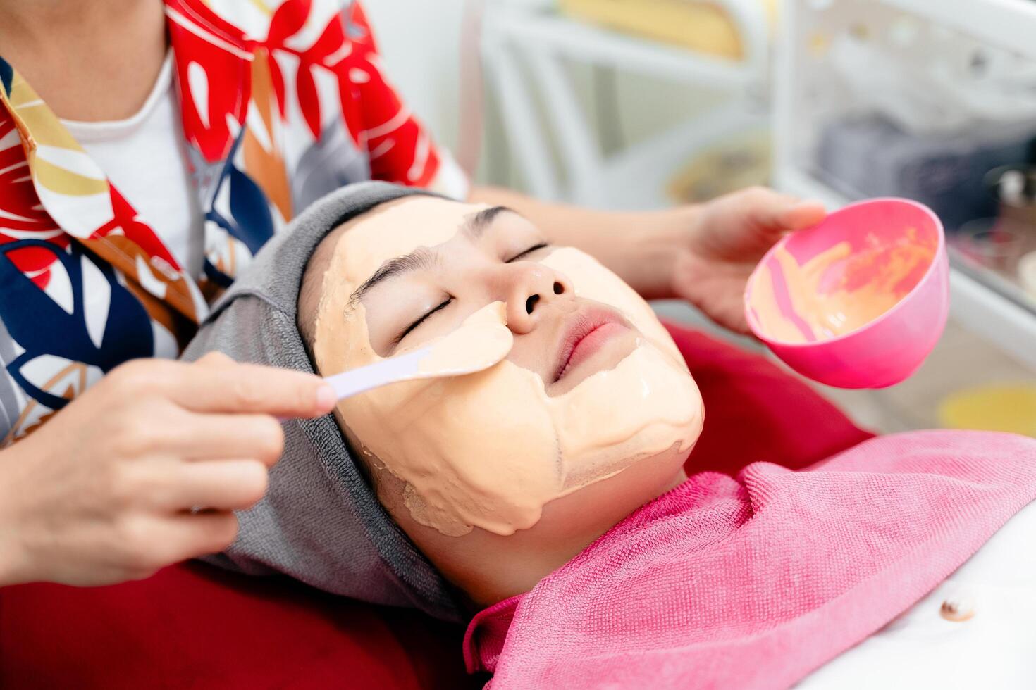 Beautiful young Asian woman getting a facial mask treatment at the beauty salon. Facial skincare. photo