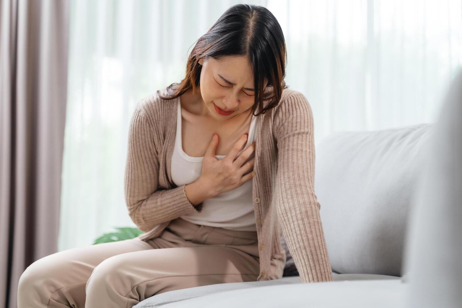 A woman is sitting on a couch with her hand holding on her chest, suffering from a heart attack. photo