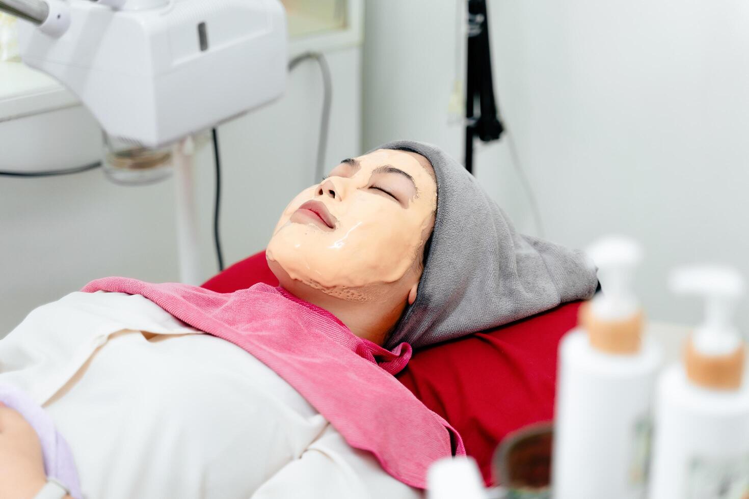 Beautiful young Asian woman getting a facial mask treatment at the beauty salon. Facial skincare. photo
