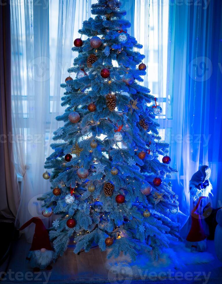 Beautiful Christmas tree with lights and ribbons. Amazing fir tree decorated with Christmas balls near the cozy window in the living-room. photo