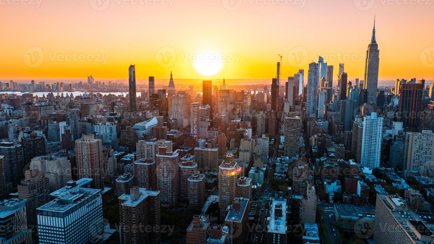 Orange light of setting sun illuminating the skyscrapers and high-rise buildings in New York scenery. Top view on the metropolis from above the East River. photo