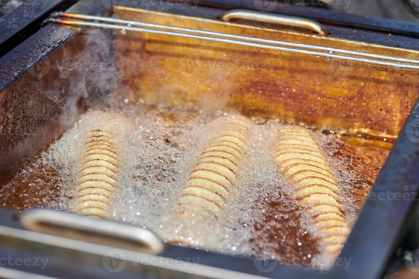 Cooking spiral fried potato in boiling oil, rich in fat and calories fast food, unhealthy delicious photo