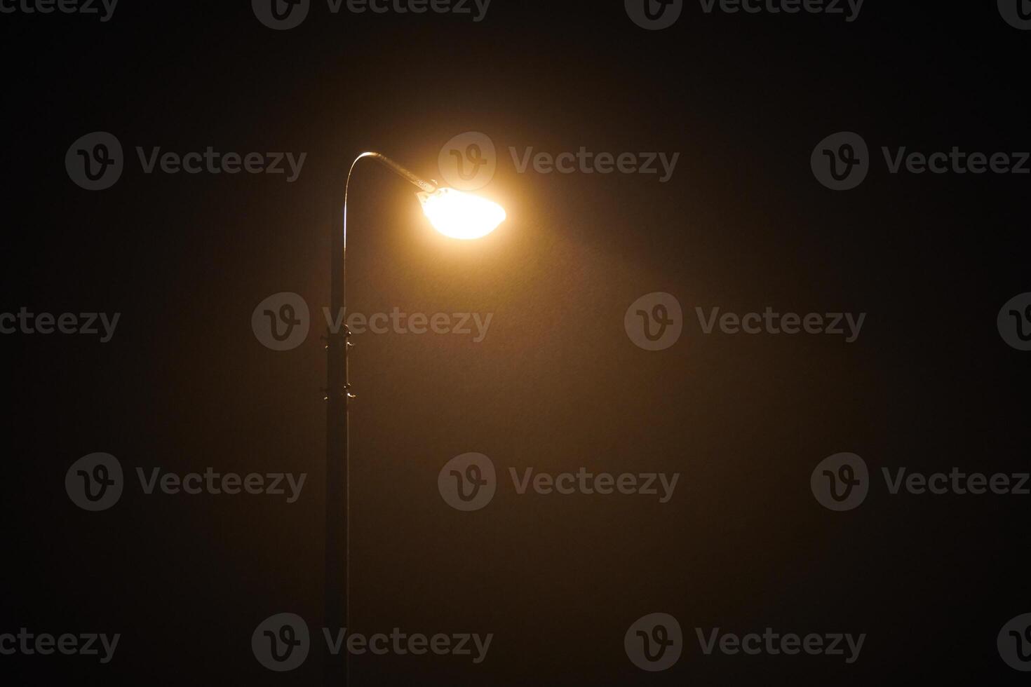 One night lamppost shines with faint mysterious yellow light through evening fog, copy space photo