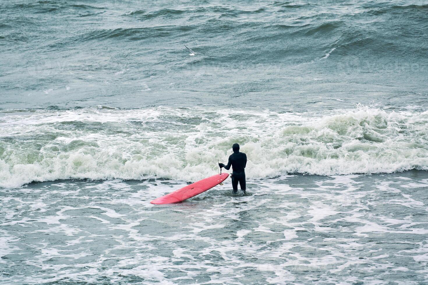 Male surfer in swimsuit in sea with red surfboard photo