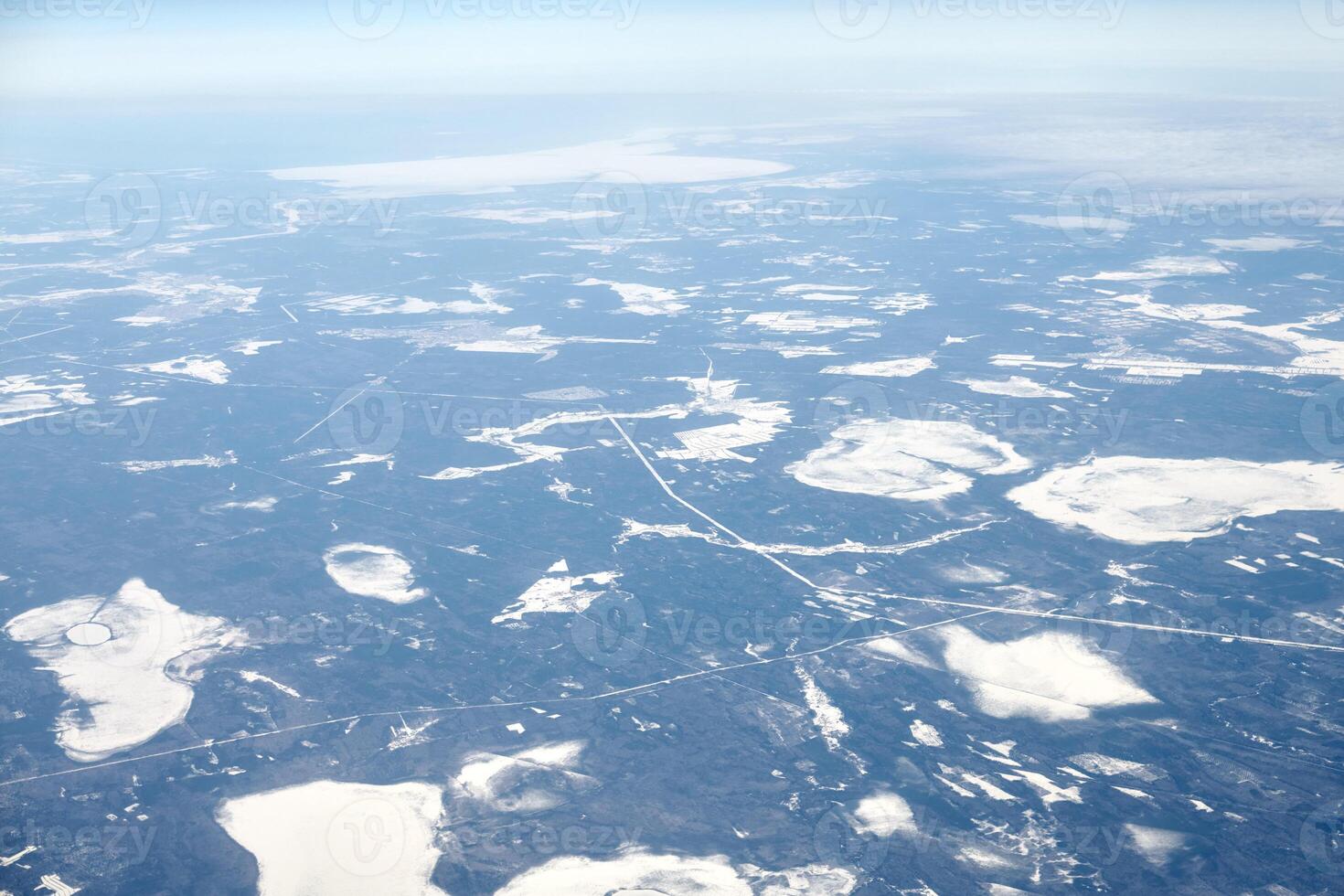 Aerial view from airplane window over clouds top to snow covered rivers, fields and roads photo
