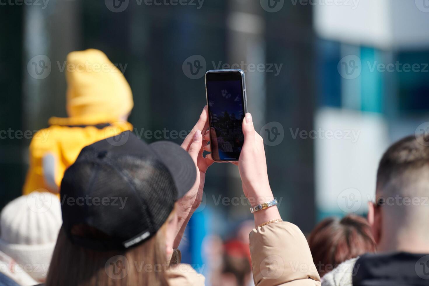 Long haired woman in cap taking photos on phone, back view. Shooting with cell phone camera