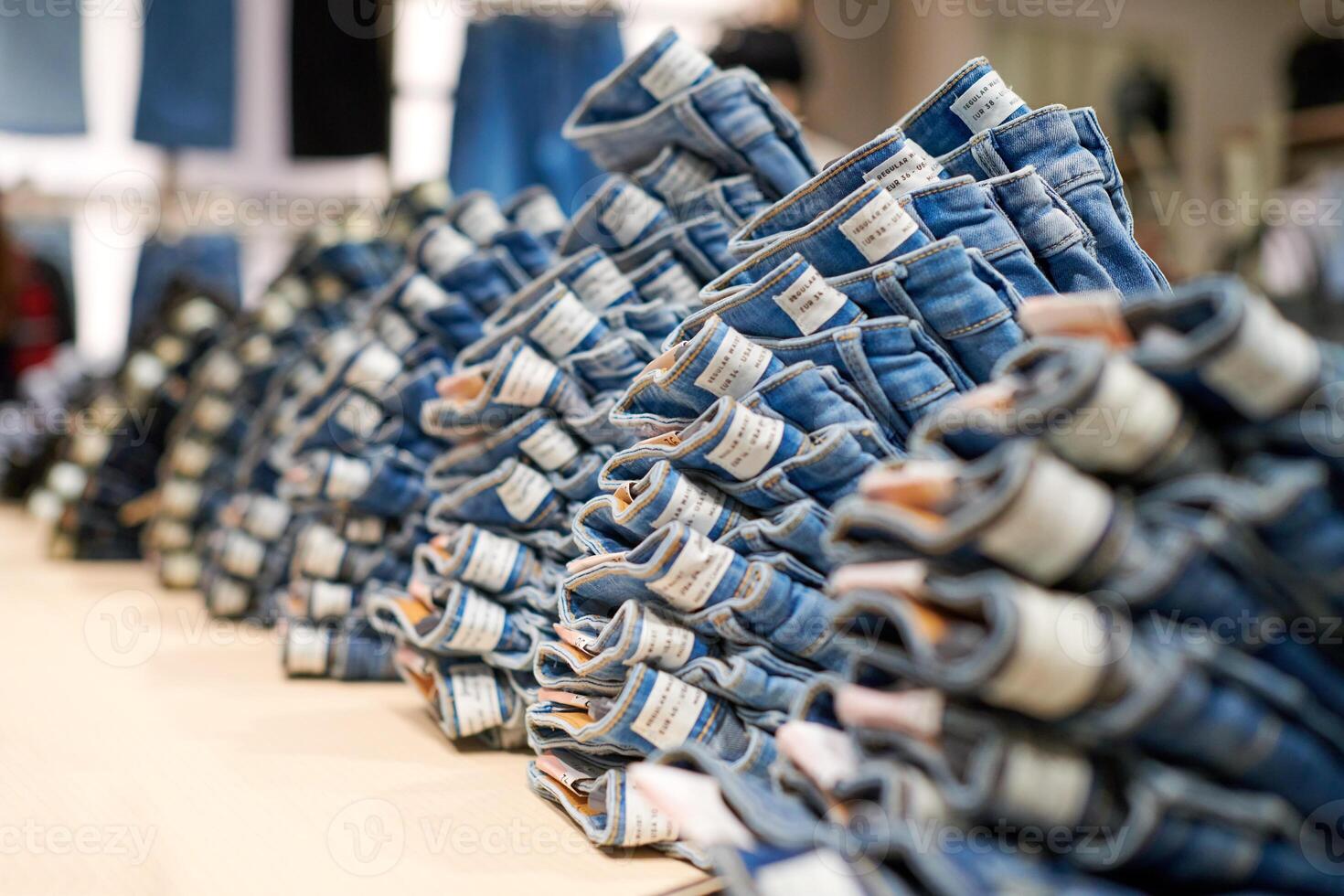 Denim jeans stack on wood table in clothing store, shopping photo