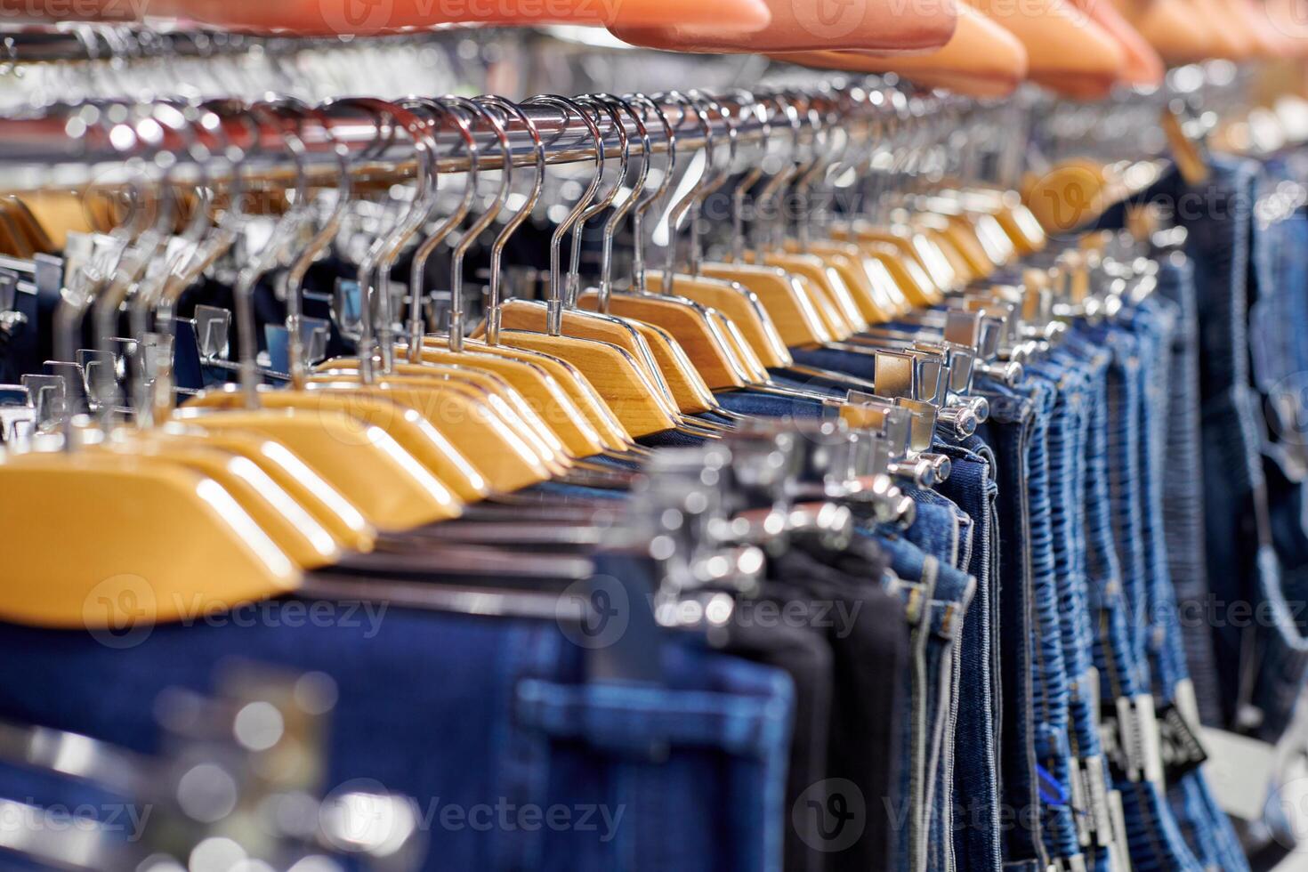Many denim jeans hanging on wooden hangers, shopping concept photo
