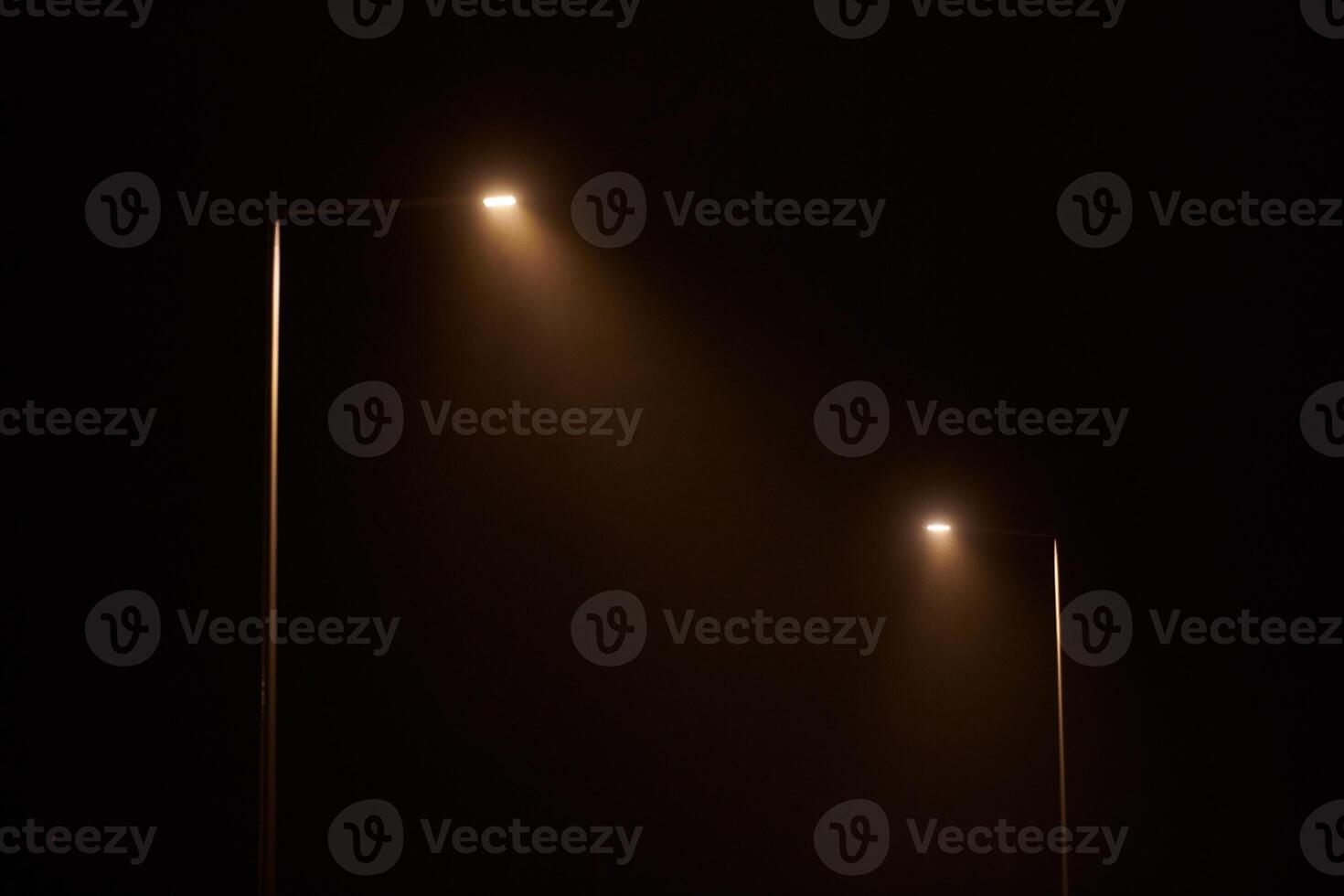 Two night lamppost shines with faint mysterious yellow light through evening fog at quiet night photo