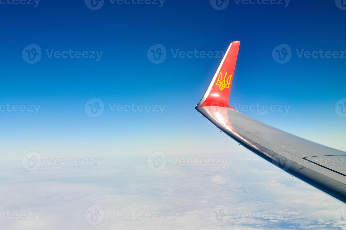 Airplane wing with coat of arms of Ukraine over clouds aerial top view from aircraft window photo