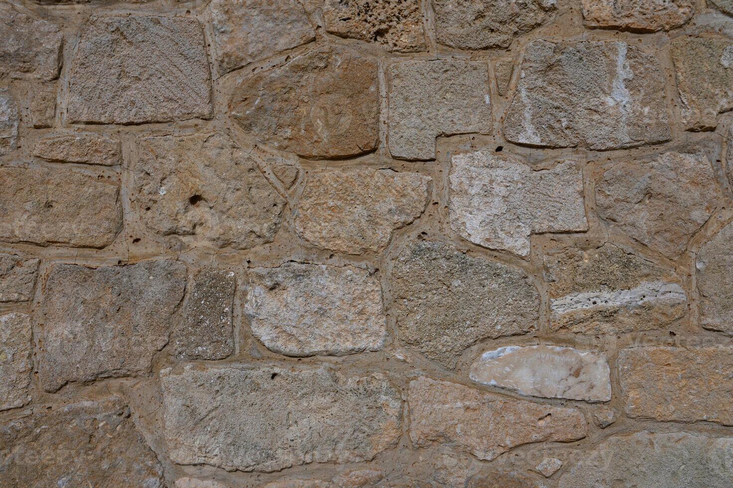 Light brown stone wall in panoramic close-up made of old, roughly hewn, different natural stones photo