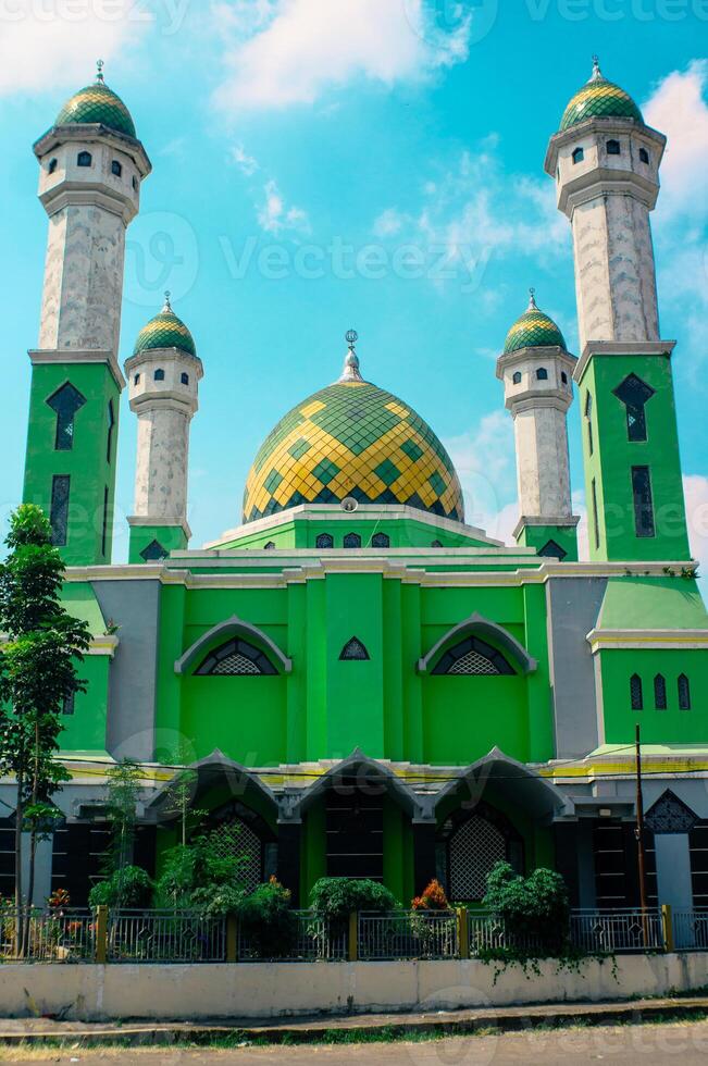Green mosque with trees in the yard and bright blue sky photo