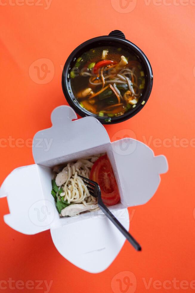 Noodles with pork and vegetables in take-out box on wooden table photo