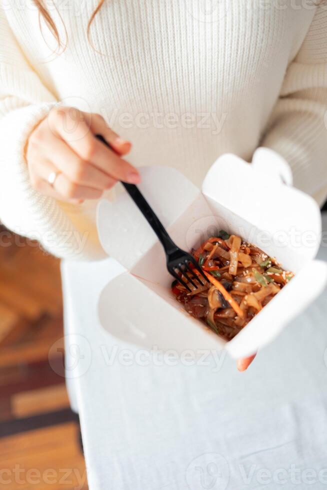 Noodles with pork and vegetables in take-out box on wooden table photo