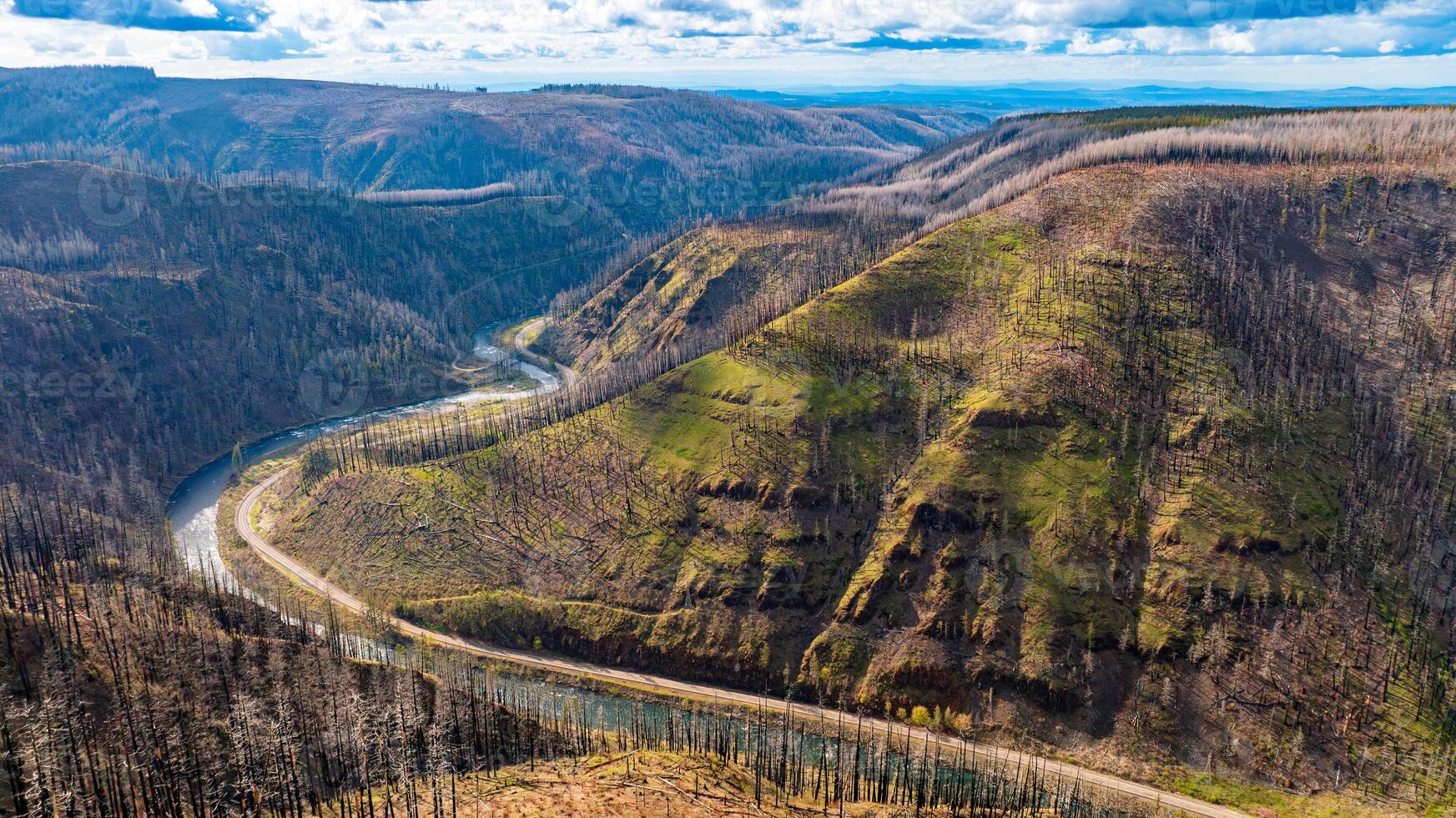 Stunning steep rocks in the Oregon State at daytime. Highway with moving car goes around the mountain. Dry pine trees covering the mountains. Top view. photo