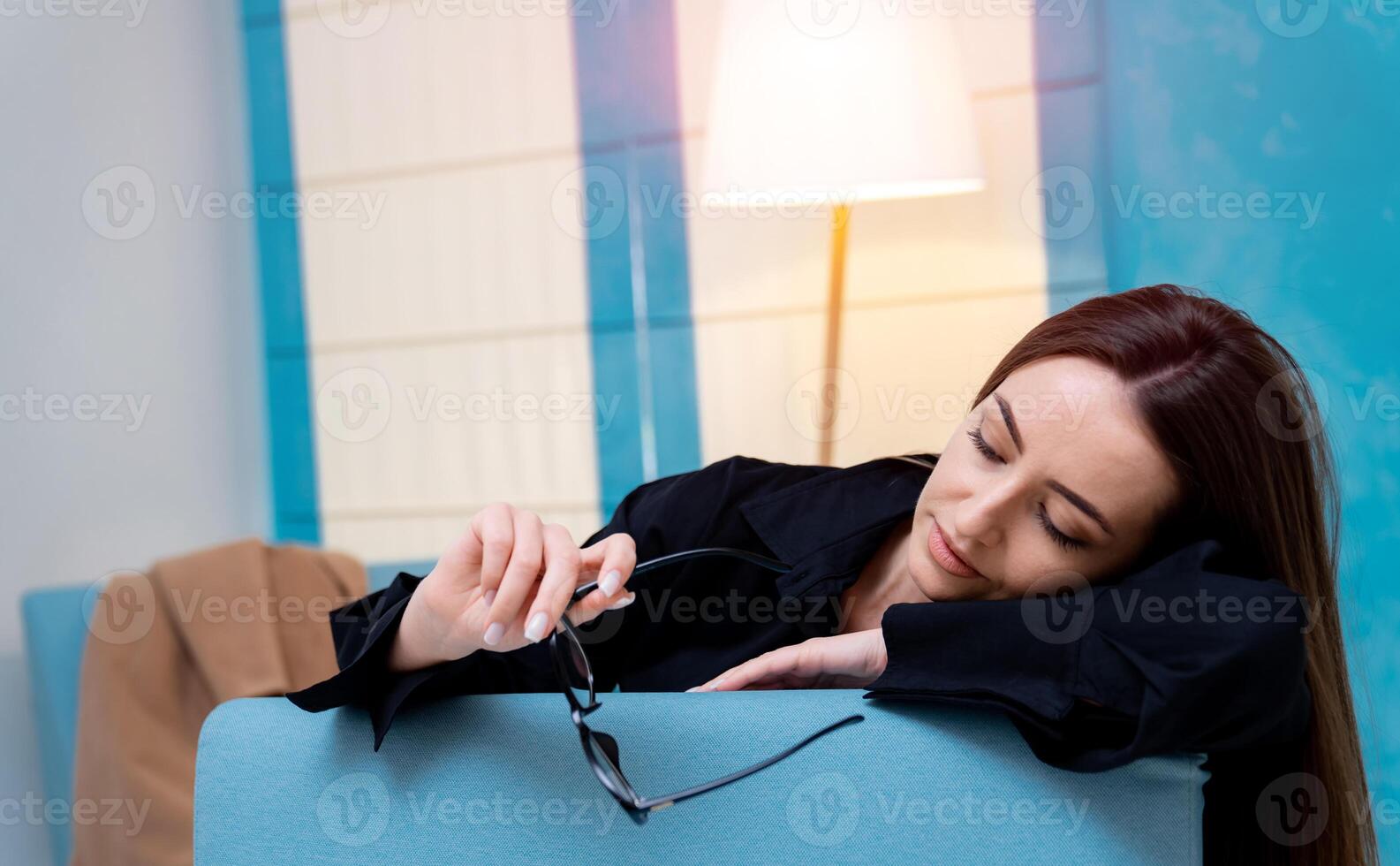 Young attractive girl posing in a black shirt in a ligth interior. Portrait of elegant woman with glasses in hand leaned on chair. Closeup. photo