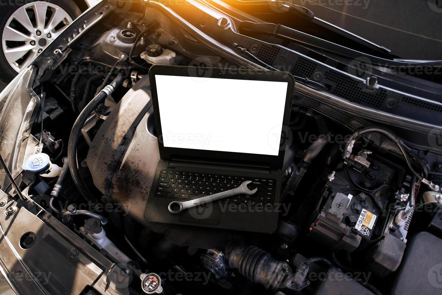A laptop with a blank white screen and a wrench on a car engine , Car repair and car maintenance servicing concept photo