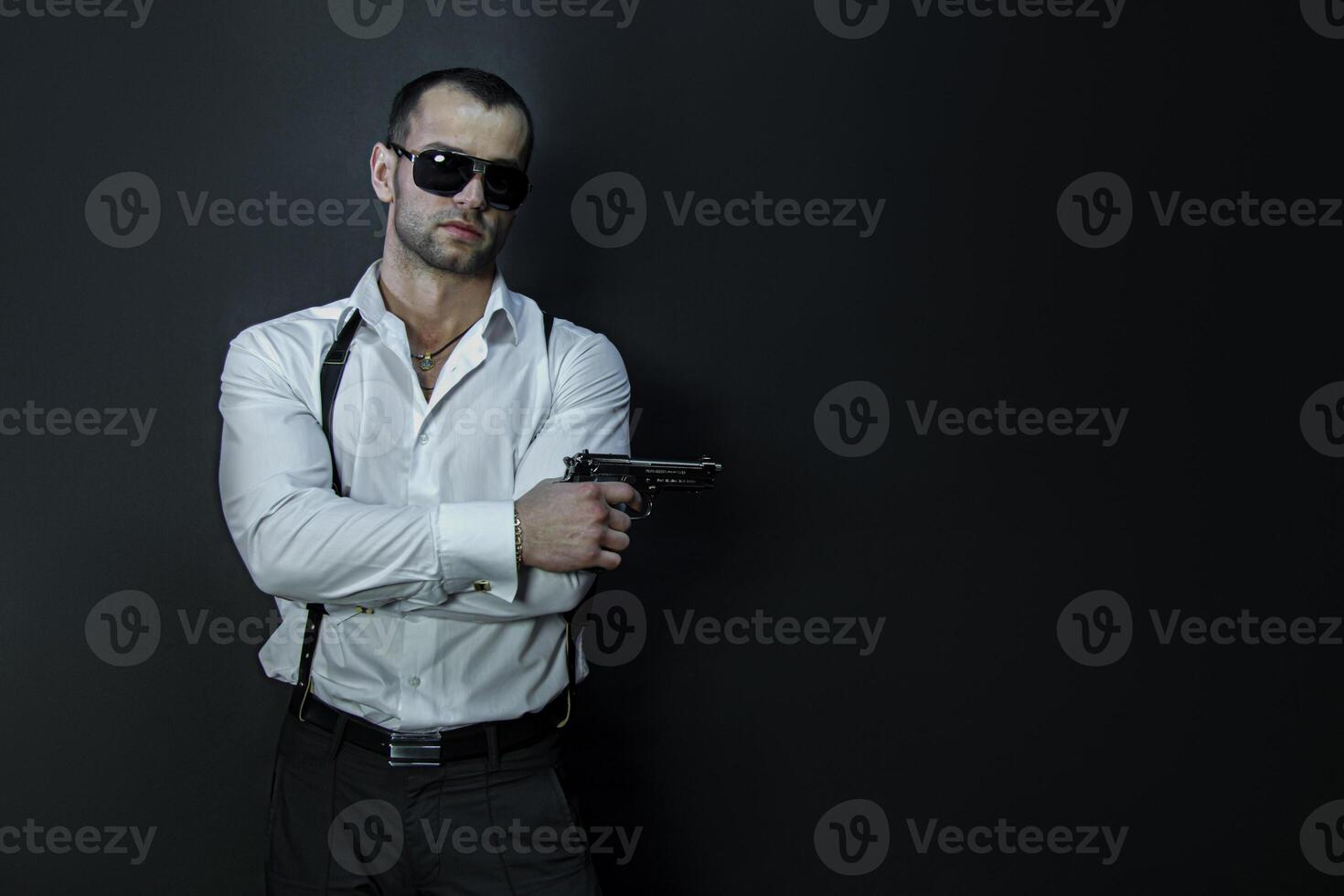 Young man in glasses wears holds a gun in his hand photo