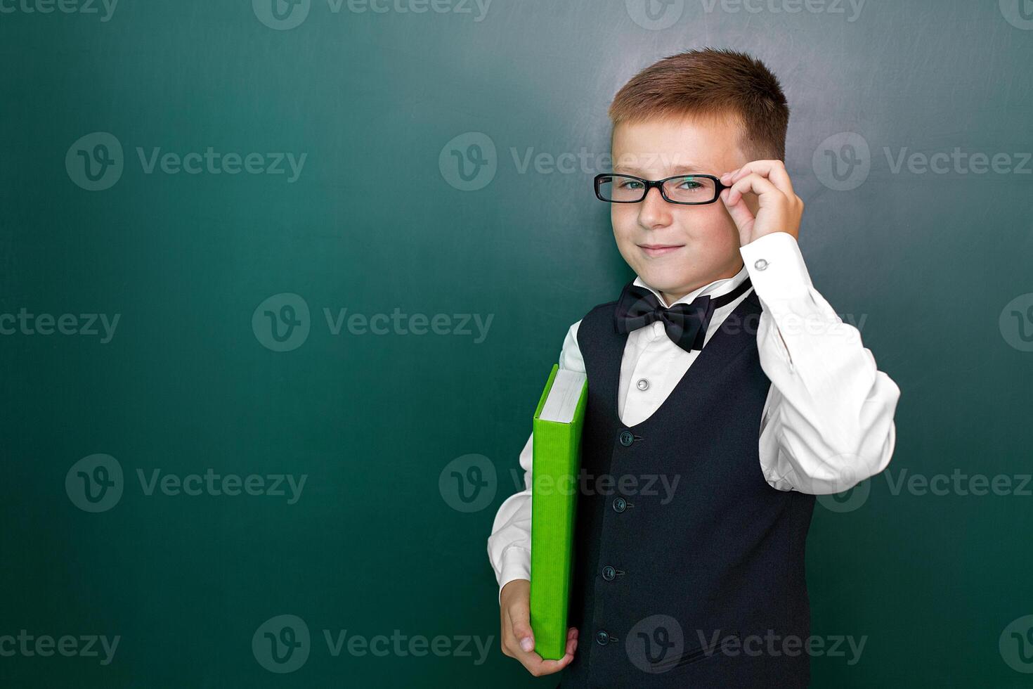 Happy cute clever boy with a bow tie and in glasses with book in his hand. First time to school. Back to school. photo