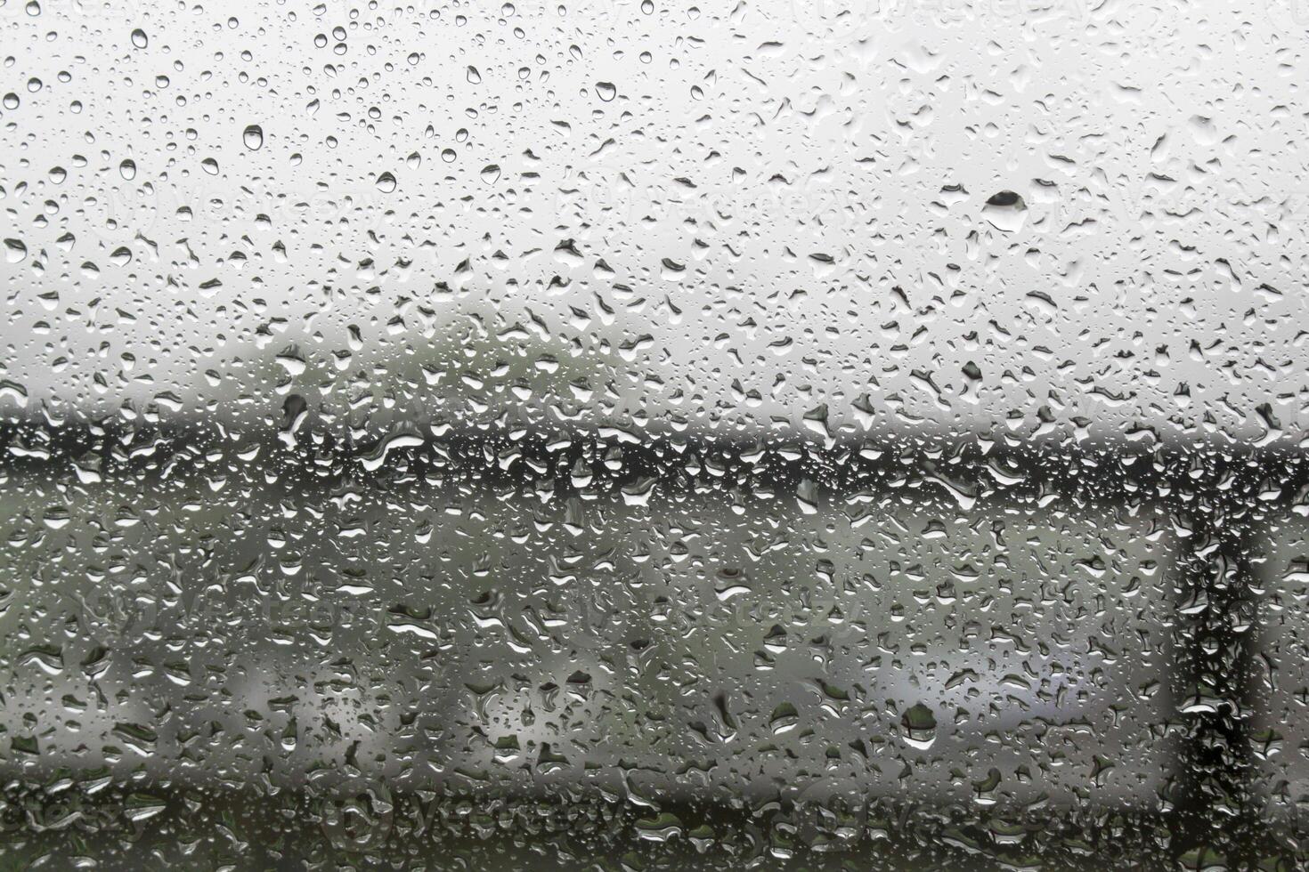 Raindrops on window pane with white mist on balcony railing background photo