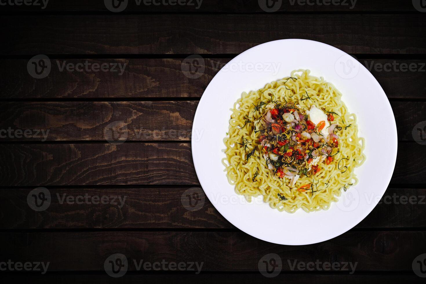 Top view of instant noodles in white bowl with added garlic and chili on dark wooden background. photo