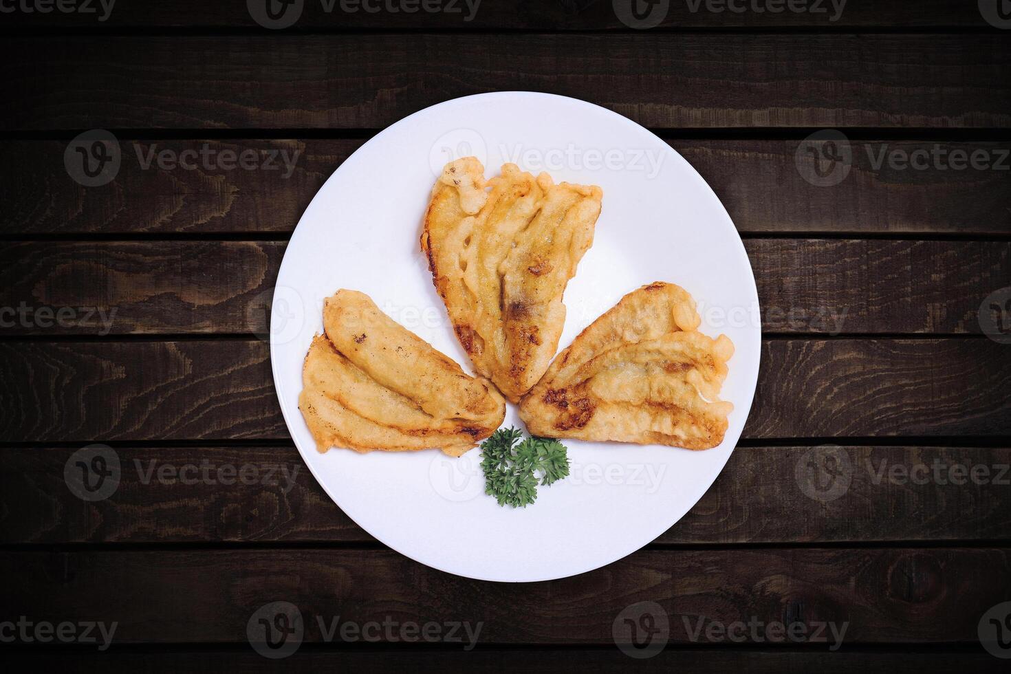 Three fried bananas on a top view white plate with a dark wood back screen. photo