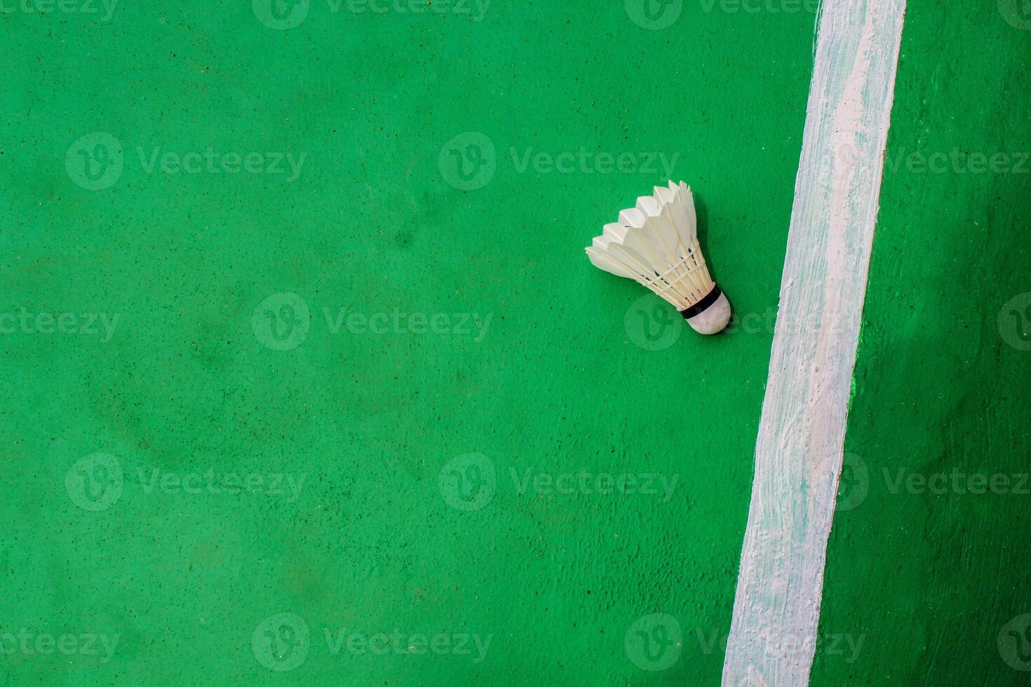 Top view. White badminton shuttlecock with a white stripe on the green floor on the right. photo