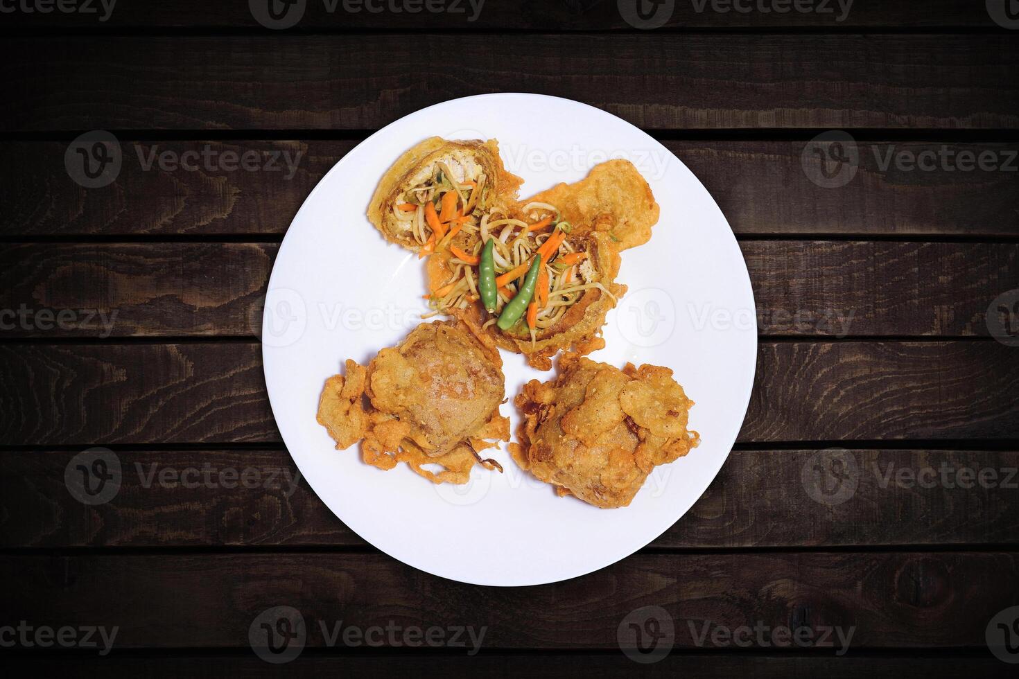 Fried tofu stuffed with vegetable filling, eaten with chilies, served on a white plate. photo
