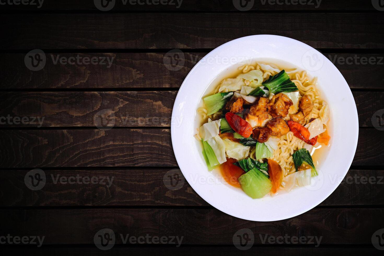 Top view of instant noodles in white bowl with vegetable toppings on dark wooden background. photo