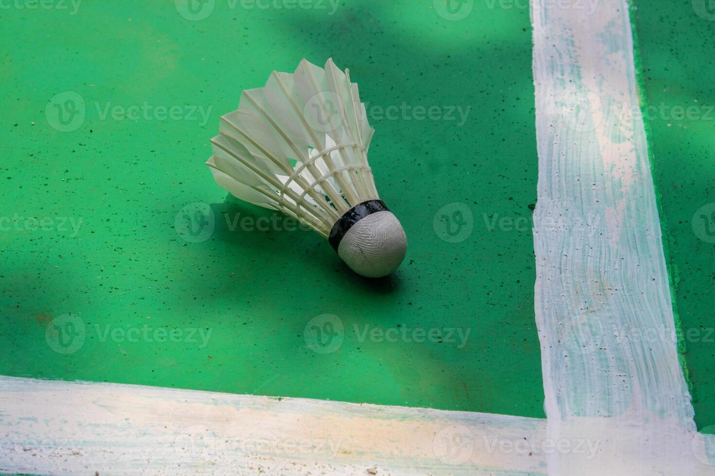 The badminton shuttlecock falls over the white line against the green field background. photo